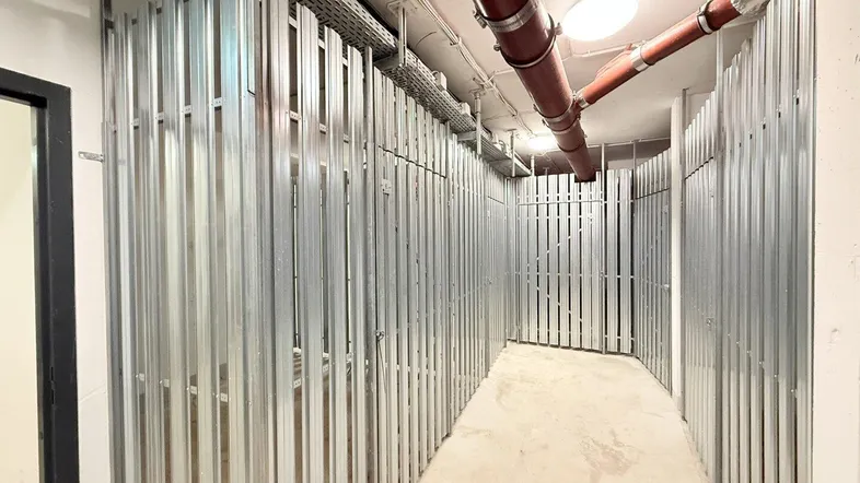 Langer Flur im Kellerbereich mit zahlreichen individuellen Lagerabteilen und sichtbaren Versorgungsleitungen an der Decke.