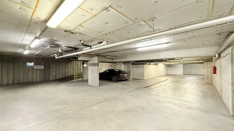 Geräumige Tiefgarage mit Betonwänden und -boden, bietet ausreichend Parkplätze und gute Beleuchtung.