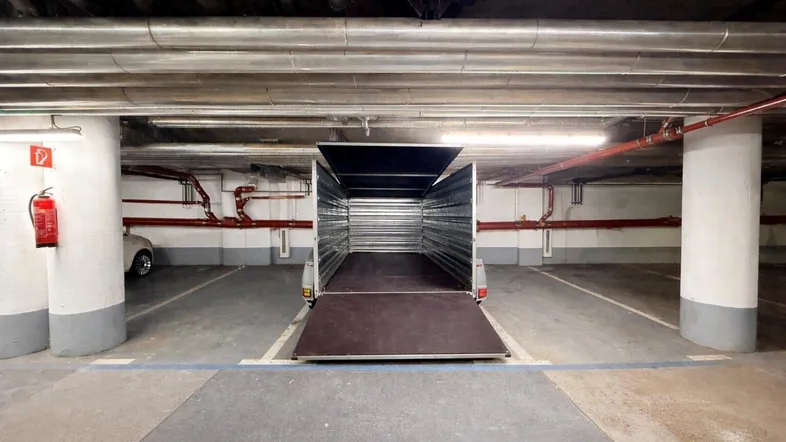 Tiefgarage mit einem Anhänger auf einem Stellplatz, gekennzeichnet durch freiliegende Rohre und Säulen.