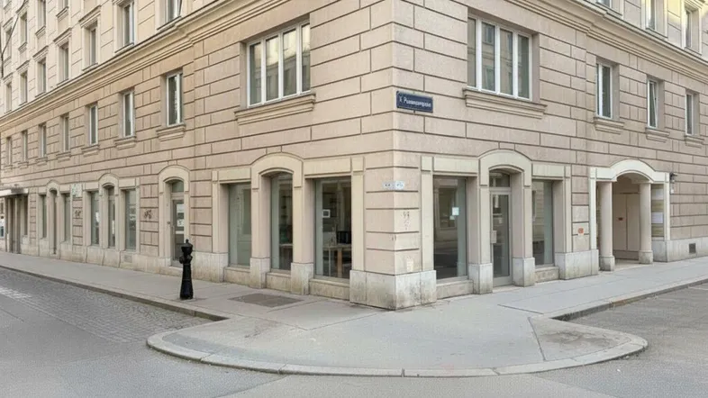 Eckgebäude mit klassischer Fassade und großen Schaufenstern im Erdgeschoss an einer städtischen Straße.