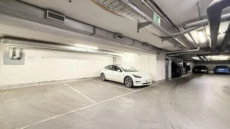 Tiefgarage mit markierten Stellplätzen, einem geparkten Elektrofahrzeug und sichtbaren Installationen an der Decke.
