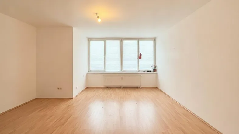 Helles, leeres Zimmer mit Parkettboden und großen Fenstern, bereit zur individuellen Gestaltung.