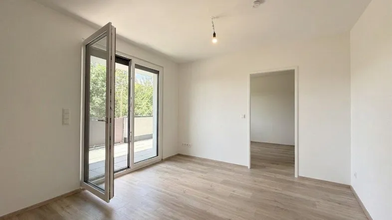 Helles Zimmer mit Holzboden und Zugang zu einem Balkon, ideal für Wohn- oder Schlafbereich.