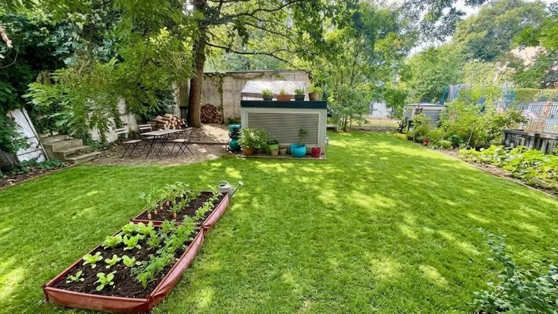 Gepflegter Garten mit Rasenfläche, Hochbeeten, Gartenhaus und Sitzgelegenheiten im Grünen.