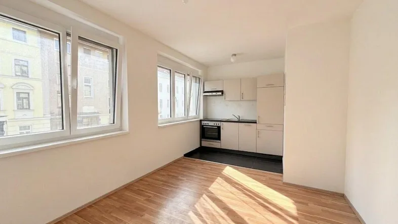 Helles Zimmer mit Holzboden und integrierter Küchenzeile, ideal für offenes Wohnen.