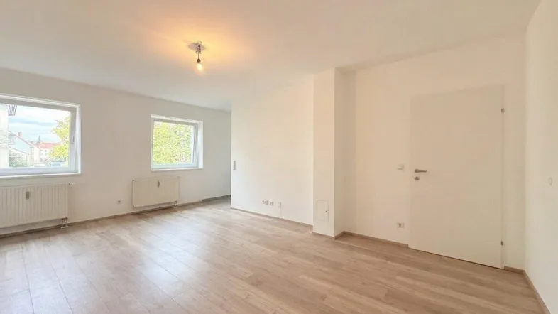 Helles, leeres Zimmer mit neuem Laminatboden und zwei Fenstern, bereit zur individuellen Gestaltung.