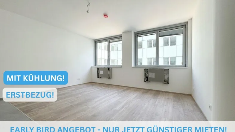Helles, leeres Zimmer mit großen Fenstern und Holzboden, bereit für den Erstbezug.