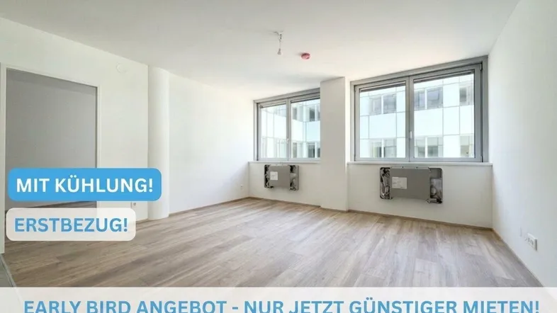 Helles, leeres Zimmer mit großen Fenstern, Holzboden und weißen Wänden, bereit für den Erstbezug.