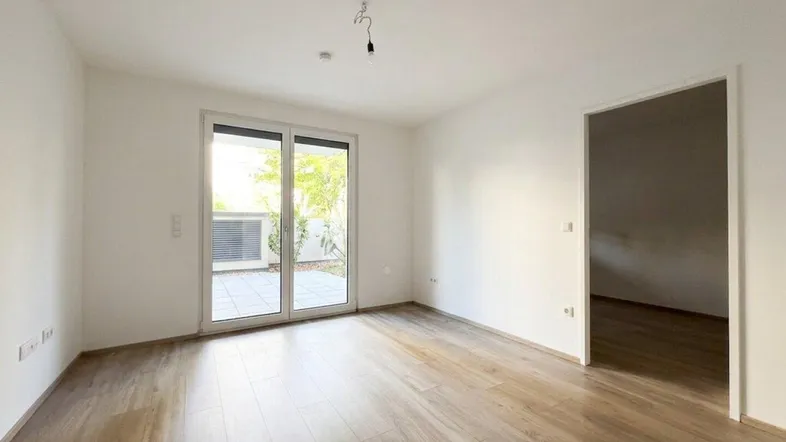 Helles, leeres Zimmer mit modernem Laminatboden und direktem Zugang zu einer Außenterrasse.