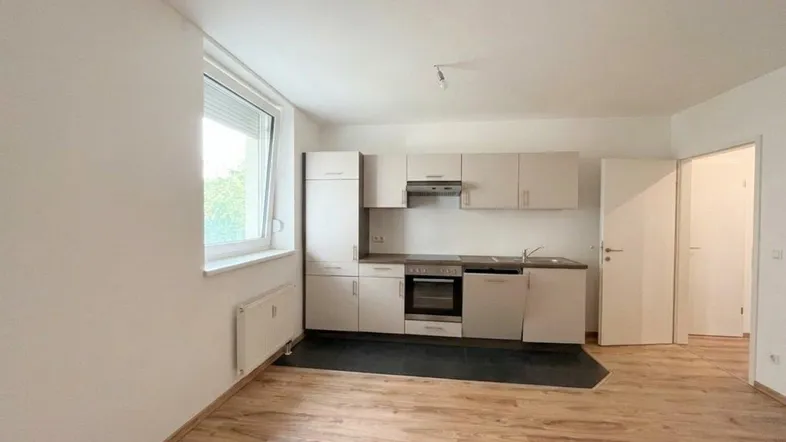 Helle, offene Wohnküche mit Laminatboden, Einbauküche und Fenster mit Blick ins Grüne.