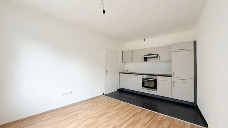 Moderne Küchenzeile mit hellen Schränken und dunklem Fliesenboden in einem offenen Raum.