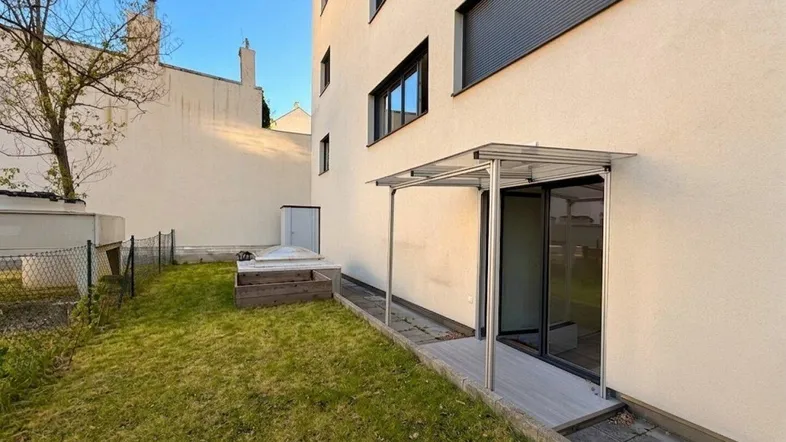 Außenbereich mit Rasenfläche, überdachtem Terrassenzugang und Hochbeet am modernen Gebäude.