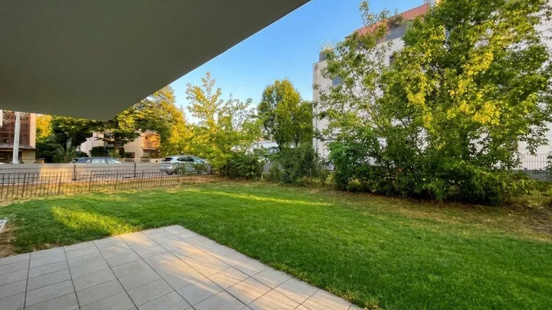 Gepflasterte Terrasse mit Rasenfläche und Bäumen im Hintergrund, ideal für Entspannung im Freien.