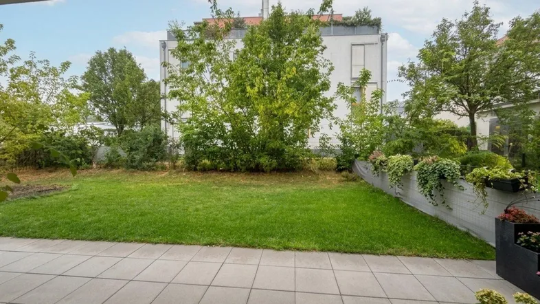 Große geflieste Terrasse mit angrenzendem Rasen und Blick auf grüne Bäume.