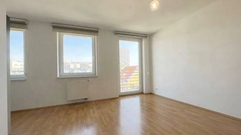 Helles Zimmer mit Parkettboden, großen Fenstern und Zugang zu einem französischen Balkon.