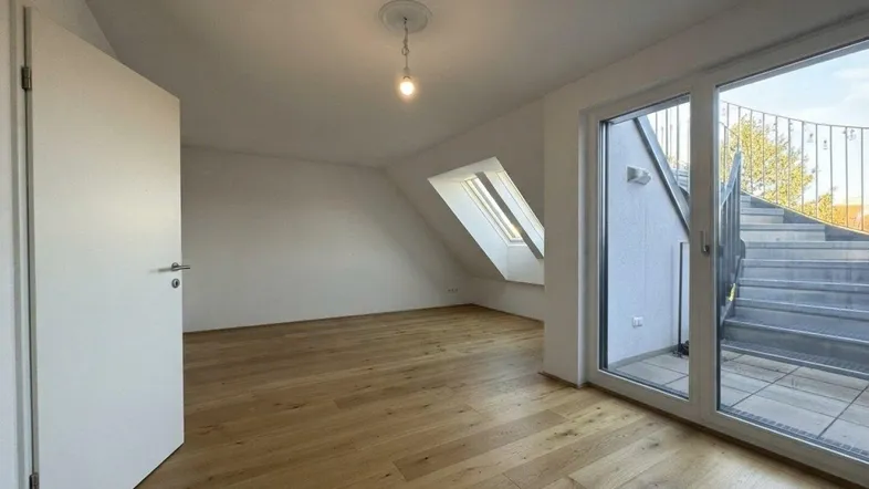 Helles Zimmer im Dachgeschoss mit Holzboden, Dachfenster und Zugang zu einer Außentreppe.