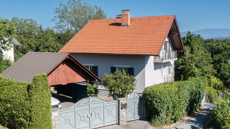 Freistehendes Einfamilienhaus mit Satteldach, Carport und umzäuntem Vorgarten unter blauem Himmel.