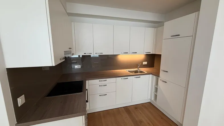 Moderne Einbauküche mit weißen Schränken, dunkler Arbeitsplatte und Induktionskochfeld.