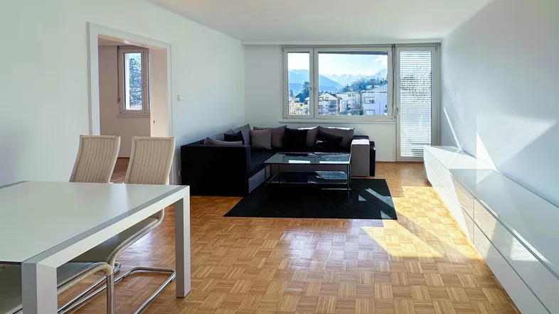Helles Wohn- und Esszimmer mit Parkettboden und Bergblick durch große Fenster.