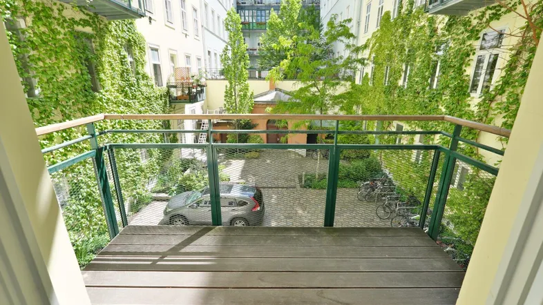 Balkon mit Holzbelag und Blick auf den begrünten Innenhof mit Parkplätzen.