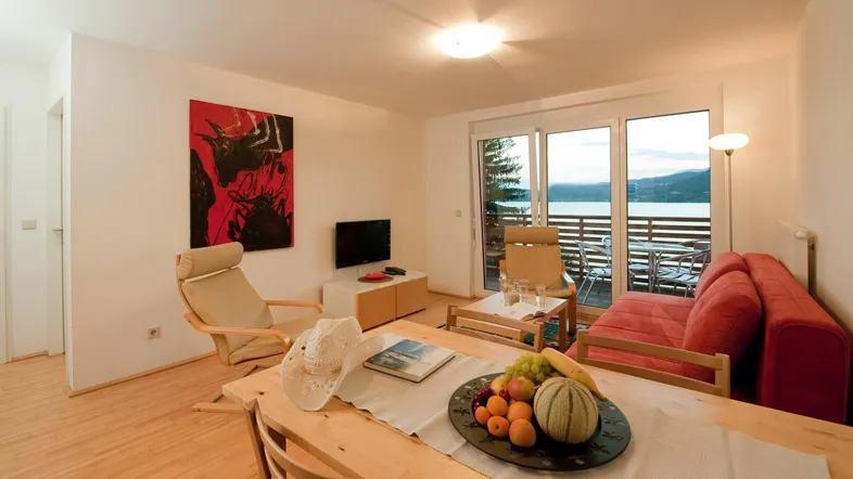 Helles Wohnzimmer mit Holzboden, gemütlicher Einrichtung und direktem Zugang zum Balkon mit Seeblick.
