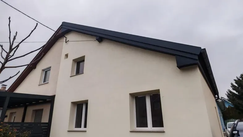 Außenansicht eines Einfamilienhauses mit heller Fassade und dunklem Dach unter bewölktem Himmel.