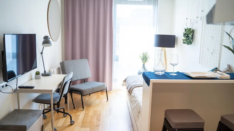 Heller Wohnbereich mit Schreibtisch, Bett und Zugang zu einem Balkon.