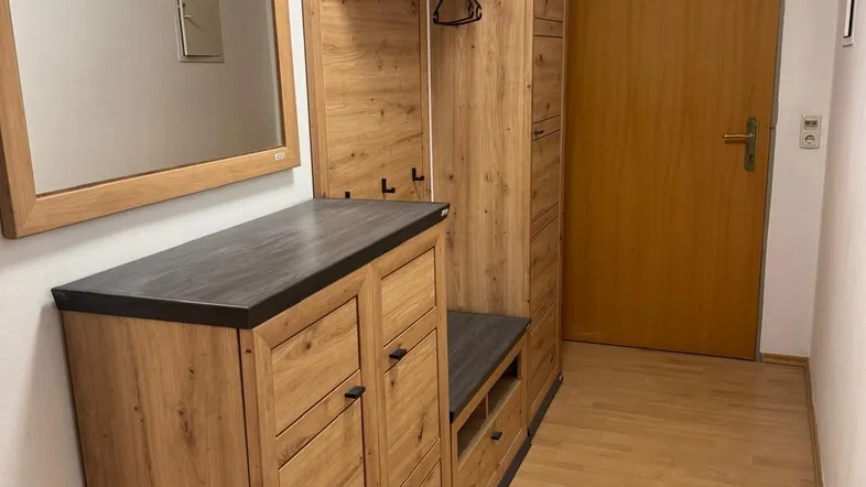 Heller Flur mit Holzmöbeln, Spiegel und Garderobe, der zu weiteren Räumen führt.