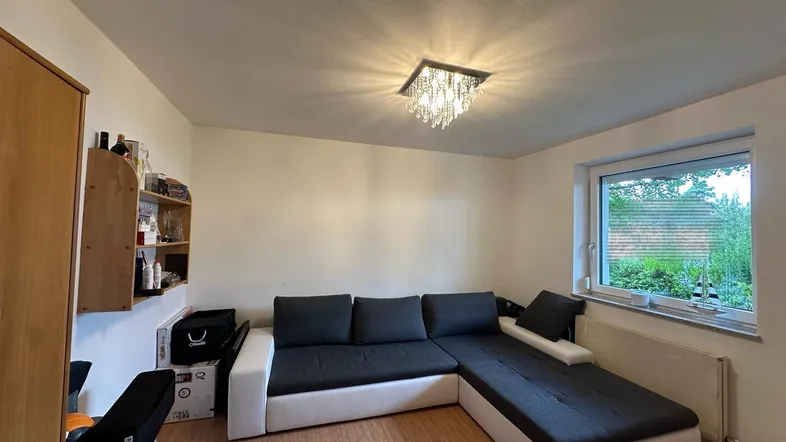Helles Wohnzimmer mit L-förmigem Sofa, Laminatboden und Blick ins Grüne.