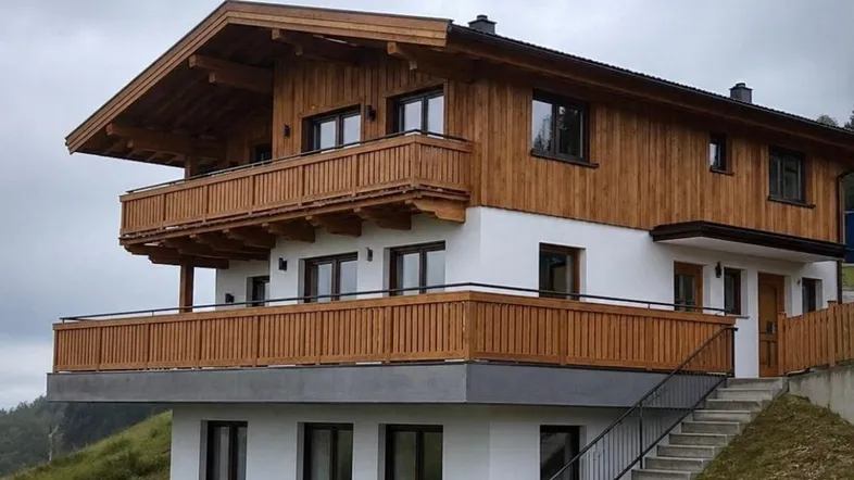 Modernes Chalet mit Holzfassade, mehreren Balkonen und Blick ins Grüne, eingebettet in die alpine Landschaft.