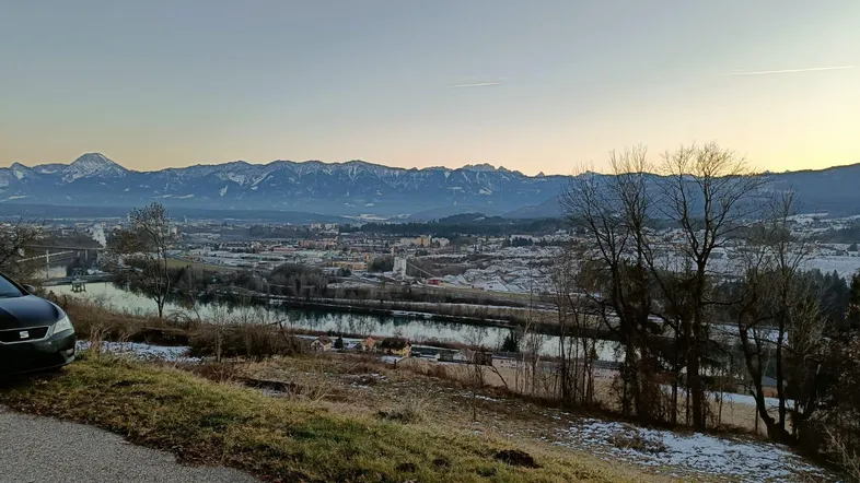Panoramablick auf die verschneite Landschaft mit Fluss, Stadt und majestätischen Bergen im Hintergrund.