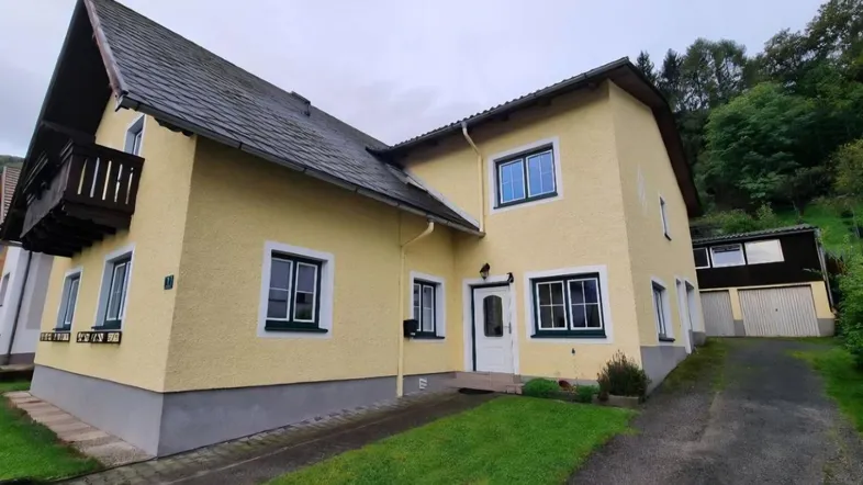 Gelbes Einfamilienhaus mit Satteldach, Balkon und Zufahrt im Grünen gelegen.
