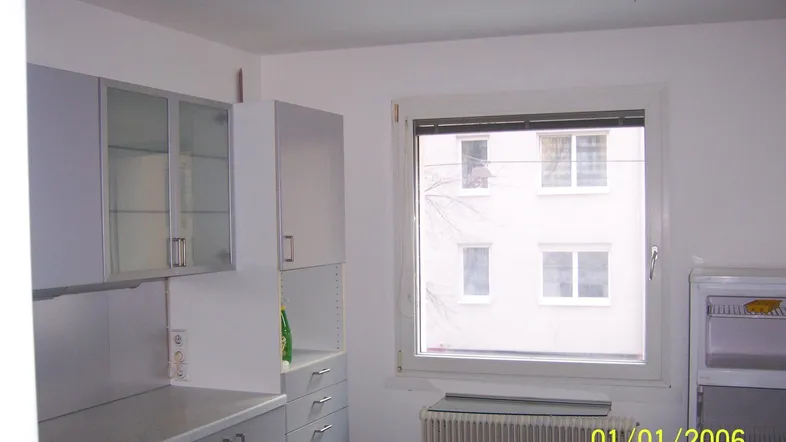 Helle Küche mit grauen Schränken, Fensterblick auf ein Gebäude und einem Heizkörper.