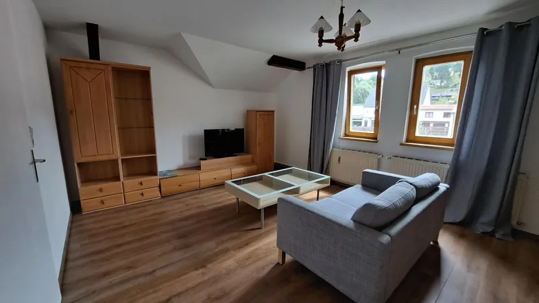 Helles Wohnzimmer mit Holzboden, gemütlichem Sofa, TV-Möbeln und einem Einzelbett unter der Dachschräge.