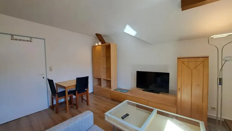 Gemütlicher Wohn-Essbereich mit Holzboden, bequemer Couch und einem kleinen Esstisch unter Dachschrägen.