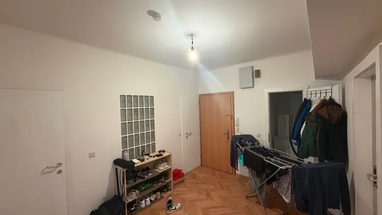 Funktionaler Eingangsbereich mit Fischgrätparkett, Schuhregal und Garderobe, beleuchtet durch eine Deckenlampe.