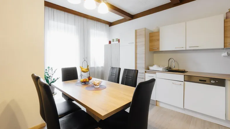 Heller Wohn- und Essbereich mit Holzbalken an der Decke und integrierter Küchenzeile.