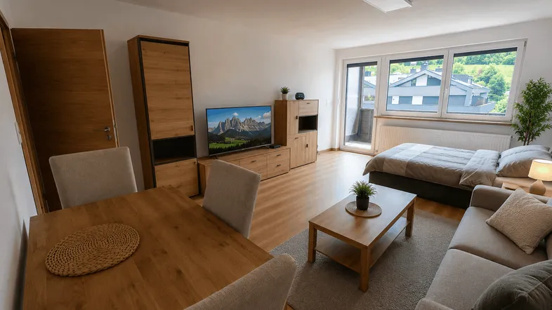 Helles, offenes Wohn- und Schlafzimmer mit Essbereich, Holzboden und Bergblick vom Balkon.