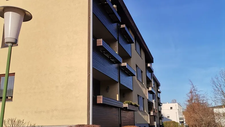 Mehrfamilienhaus mit gelber Fassade, braunem Dach und Balkonen unter strahlend blauem Himmel.