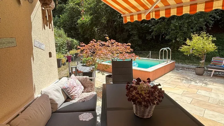 Gemütliche Terrasse mit bequemen Sitzmöbeln, Markise und kleinem Pool im Hintergrund.