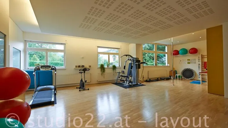 Geräumiger Fitnessraum mit verschiedenen Trainingsgeräten und großen Fenstern, die viel Tageslicht hereinlassen.