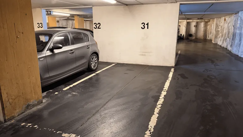 Tiefgarage mit nummerierten Stellplätzen und einem geparkten grauen Auto.