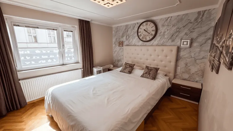 Helles Schlafzimmer mit Parkettboden, großem Bett und dekorativer Wandgestaltung sowie Stuckdecke.