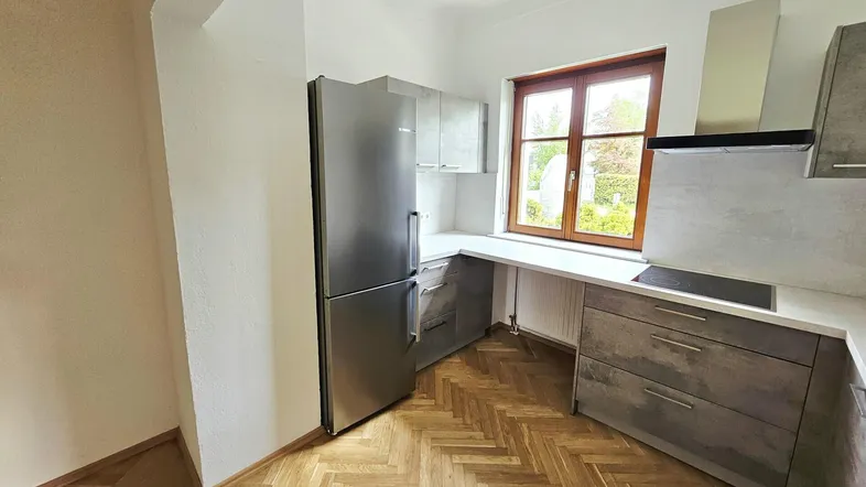Moderne Küche mit grauen Schränken, Edelstahlgeräten, einem Fenster und Fischgrätparkettboden.