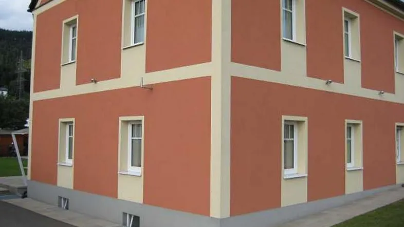 Das Gebäude präsentiert sich mit einer orangefarbenen Fassade und weißen Fensterrahmen.