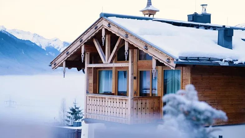 Nahaufnahme eines verschneiten Holzchalets mit traditionellen Verzierungen und Bergblick.