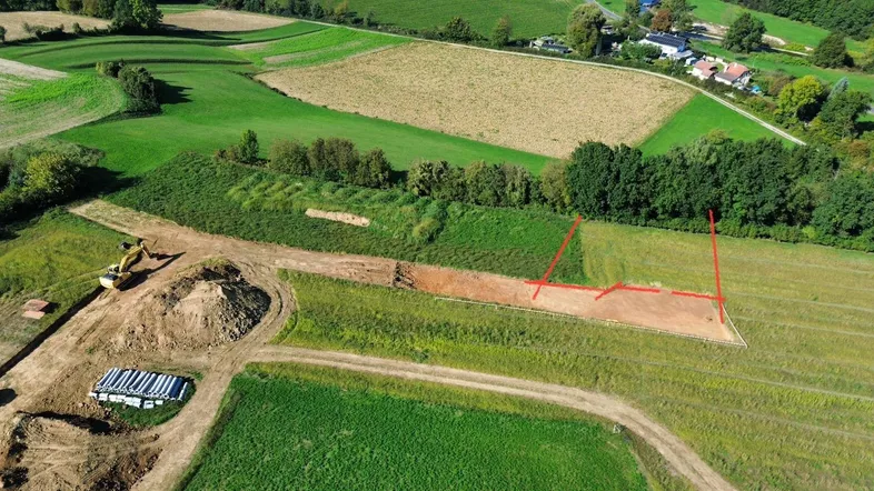 Luftaufnahme eines ländlichen Gebiets mit Feldern, Wald und einem Baugrundstück mit markierten Grenzen.
