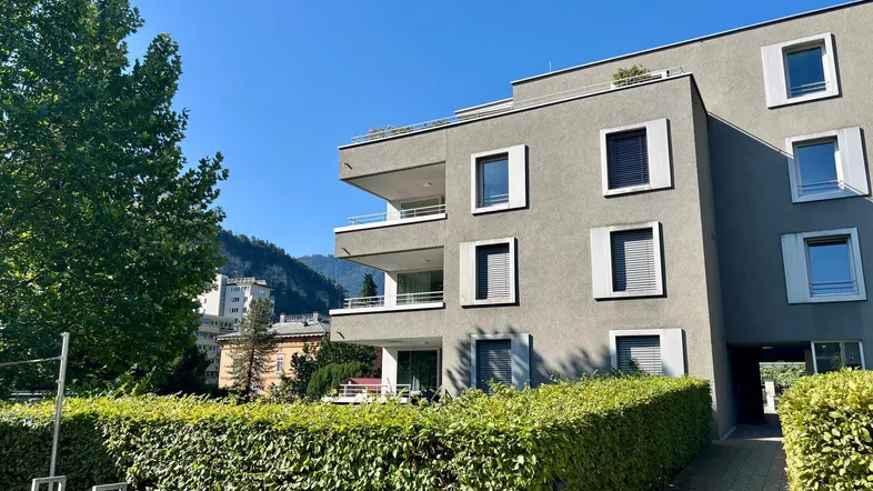 Moderne Wohnanlage mit grauer Fassade, Balkonen und gepflegter Hecke im Vordergrund.