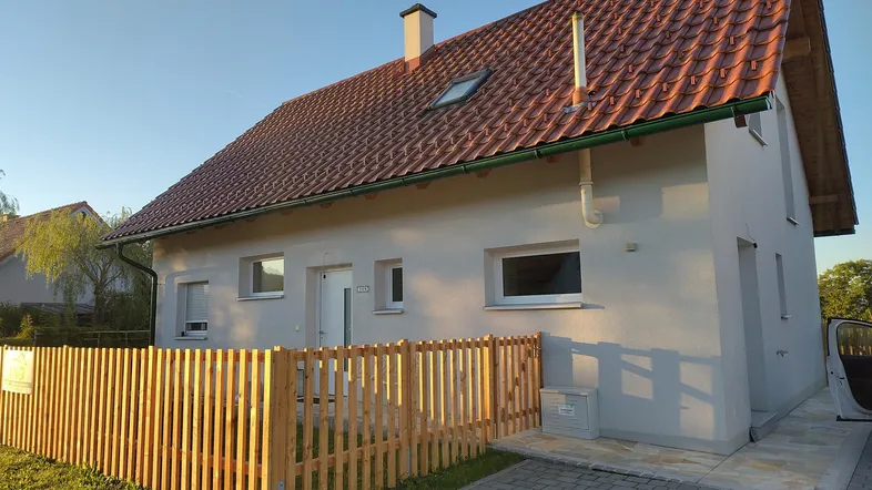 Neubau-Einfamilienhaus mit rotem Ziegeldach, heller Fassade und gepflegtem Vorgarten.