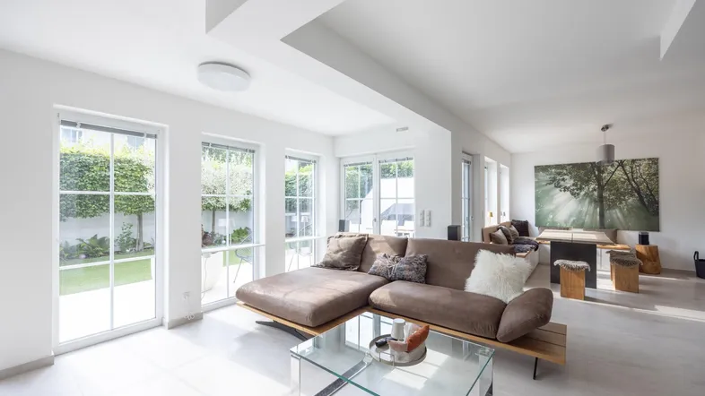 Helles und offenes Wohnzimmer mit bequemer Couch, großen Fenstern und Zugang zum Garten.